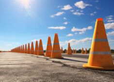 Traffic cones line up along  sunlit asphalt road.